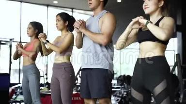 一群穿着运动服的亚洲年轻人在健身房里蹲着锻炼。 剧烈运动和健康